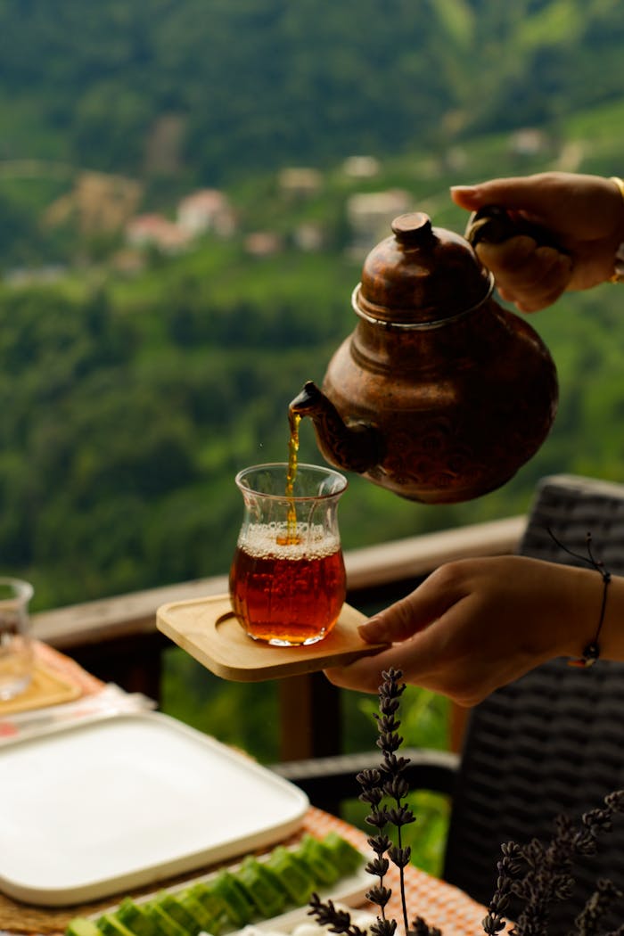 Hands pour traditional Turkish tea from kettle to glass in outdoor setting.