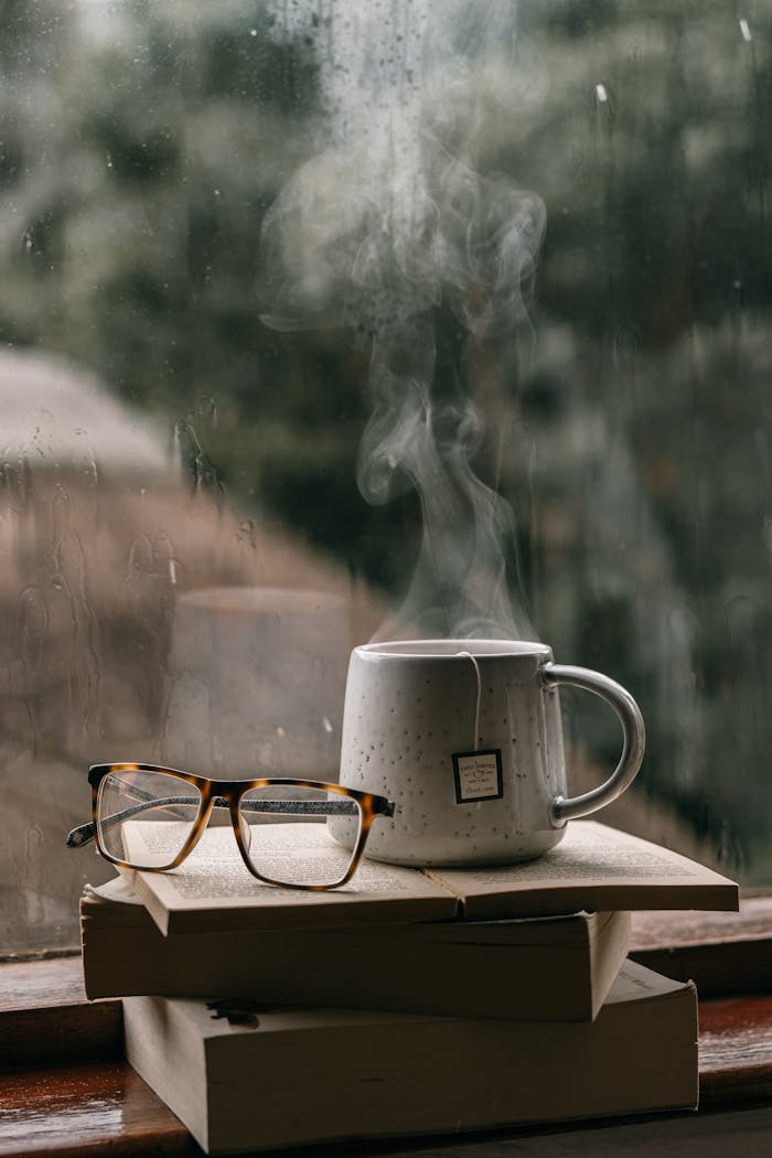services-02 Comforting setup with books, glasses, and hot tea by a rain-drenched window, perfect for reading.